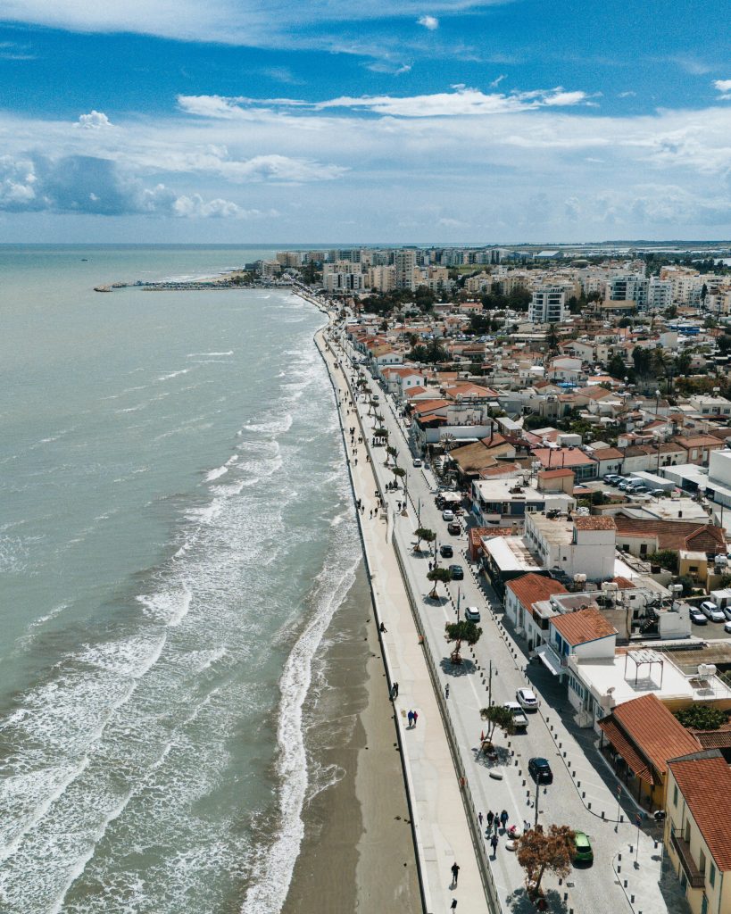 Larnaca seafront promenade in early evening with palm trees and the Phinikoudes beach, soft warm light, locals walking.